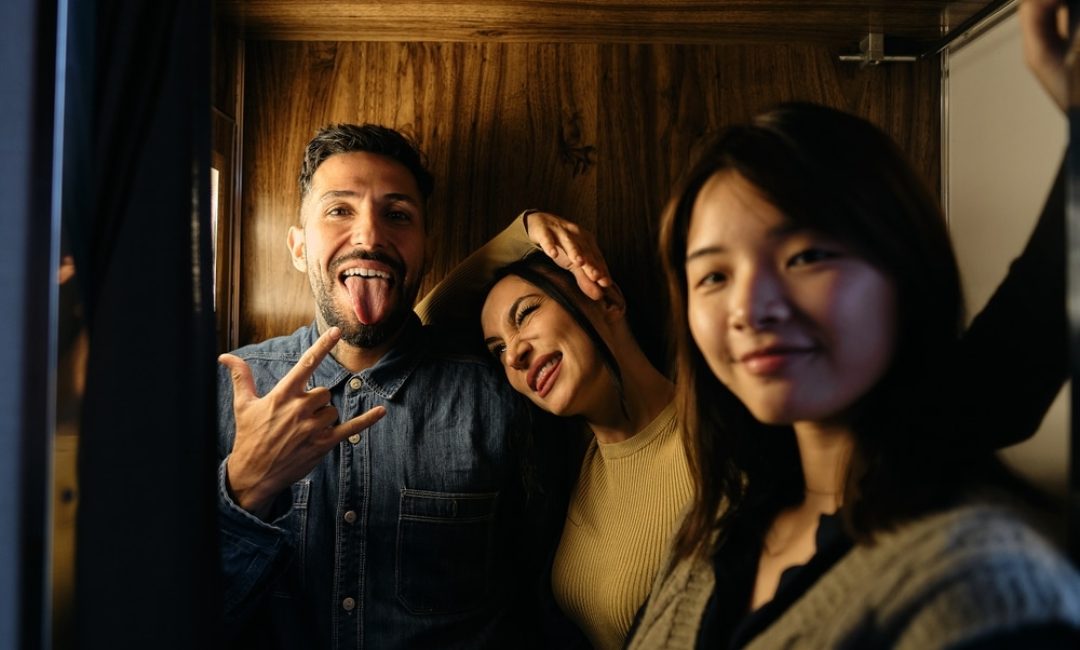Three,Young,People,Inside,The,Photobooth,Enjoying,Together